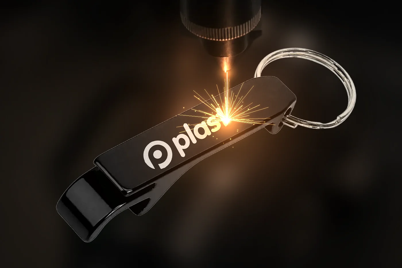 Laser gravando a marca Plastix num chaveiro abridor preto, com faíscas no ponto de gravação